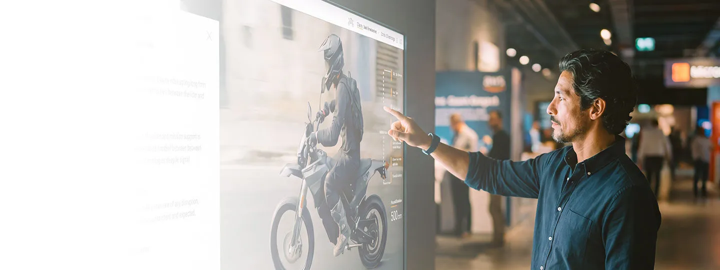 B2B buyer exploring an interactive product experience on a large touchscreen at a trade show.